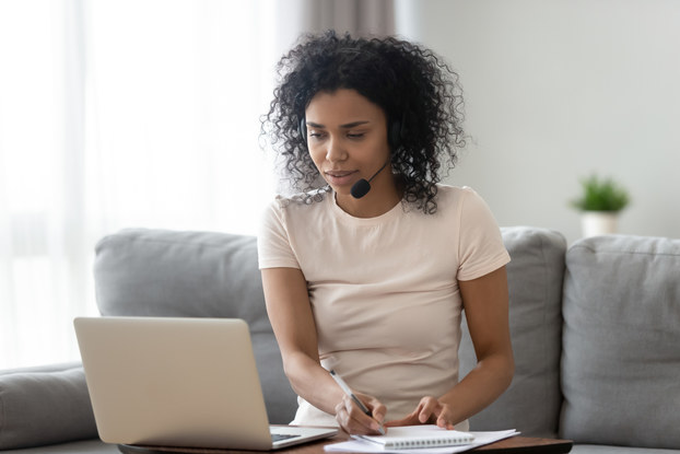 Woman at laptop takes notes while wearing a headset