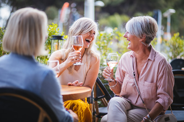 Women laugh over wine at an outdoor restaurant
