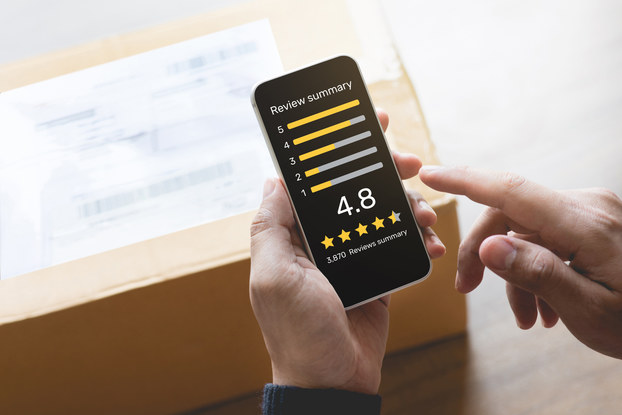Close up on a pair of hands operating a smartphone. On the phone's screen is a chart labeled "Review summary" with the amount of one- through five-star reviews measured in bars. At the bottom of the screen is the overall review score -- 4.8 -- and the corresponding number of stars.
