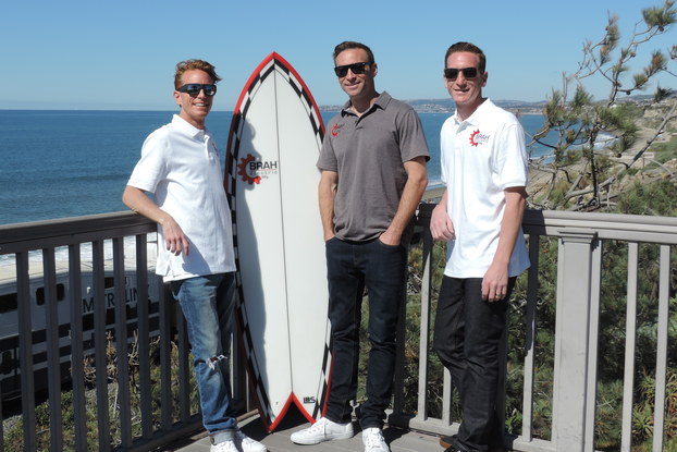 The leadership team behind Brah Electric, standing on a beachfront porch with a surfboard.