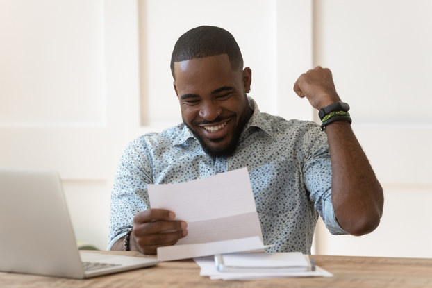 A man smiles and pumps his fist in response to something he reads on a piece of paper.