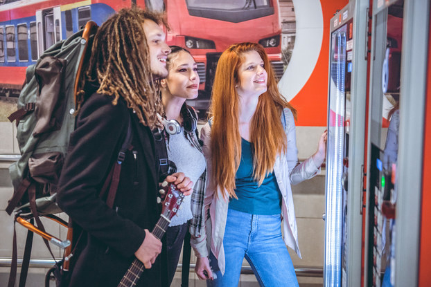 Three people trying to decide what to get from a vending machine.