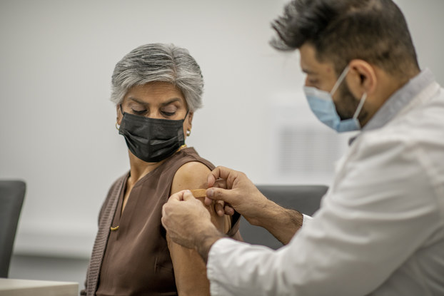 A doctor puts a band aid on a woman's arm after administering the COVID-19 vaccine injection.