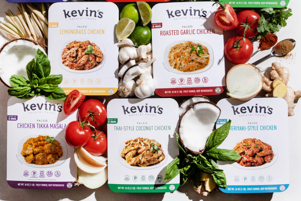 Display of Kevin's Natural Foods meals surrounded by fresh vegetables.