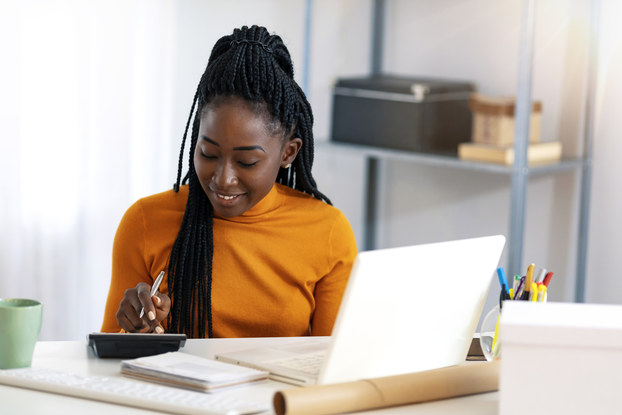 Woman doing calculations while sitting at desk with laptop.