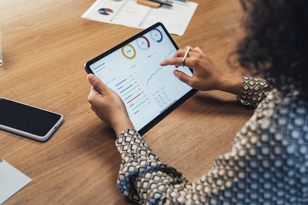 An over-the-shoulder shot of a woman examining charts and data on the screen of a tablet.