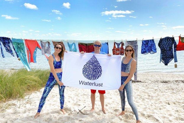 The employee team at Waterlust holding a business sign on the beach.