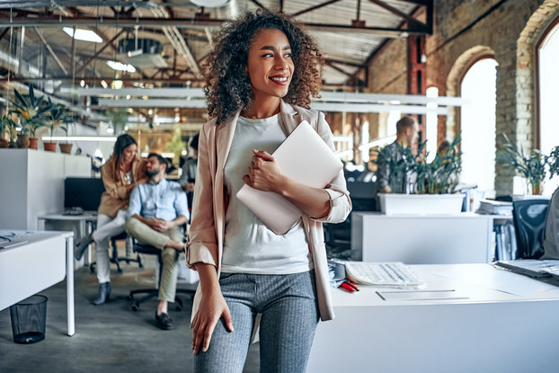 A woman stands in a modern office space, holding a file, with colleagues standing behind her.