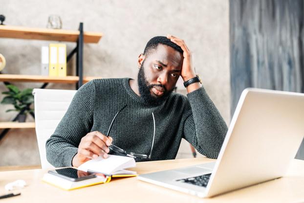 Frustrated man holds glasses and looks at laptop in an office.