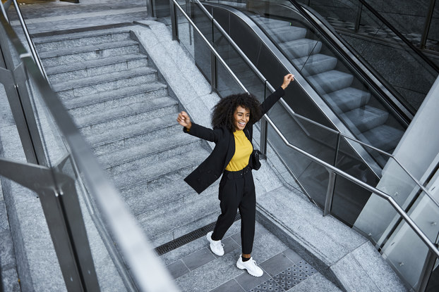 Woman leaving work happily smiling and raising her arms in the air.