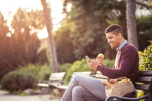 Man eating a snack while checking his phone in a park