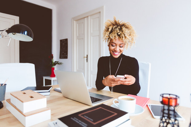 Woman smiling while sitting at her desk on her phone.