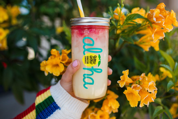 A glass jar with a straw contains a colorful beverage, held in front of orange flowers