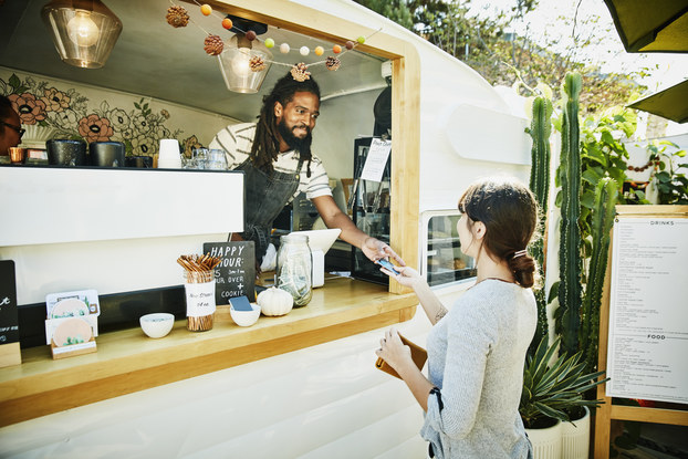 Man at mobile food truck register hands credit card back to customer.