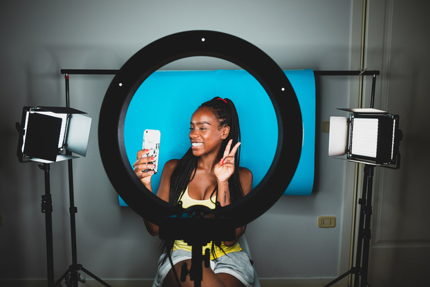 Influencer sitting in front of ring light and taking video on her phone.