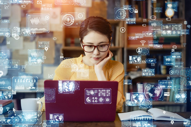 Woman working on laptop with digital images representing artificial intelligence floating around her.