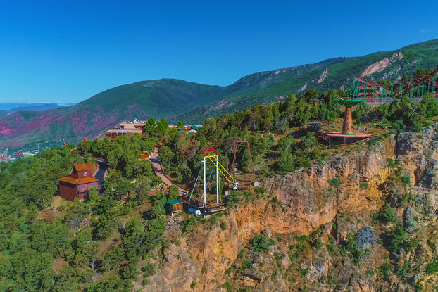 A longshot of Glenwood Caverns Adventure Park on top of a mountain in Glenwood Springs, Colorado. The park includes several wooden buildings, a roller coaster and two swinging structures.