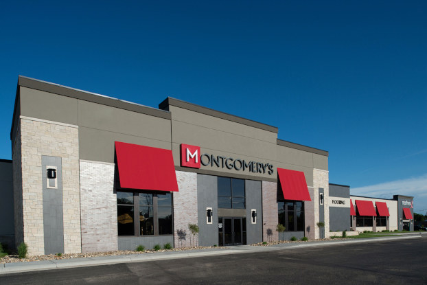 The exterior of Montgomery's furniture showroom in Watertown, South Dakota. The building is gray and white, with a smaller wing off to the right and red awnings over the windows.