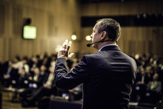 Rear view of a businessman entrepreneur giving a lecture to a sold-out crowd in a lecture hall.