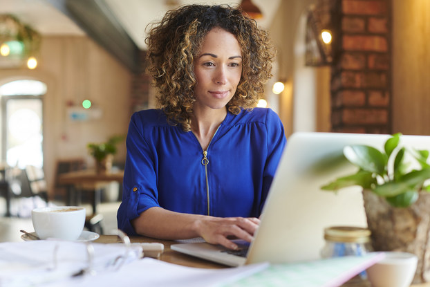 Woman works on computer with paperwork in a cafe