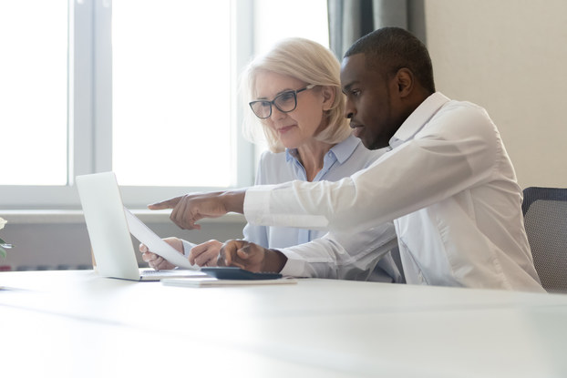 Employee pointing at laptop discussing information with colleague.