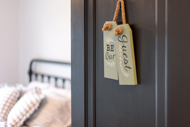 Bed and breakfast guest room with a sign on the door that says, "Be our guest."