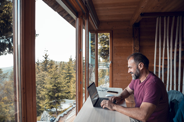 Close up of a mid-adult man working on a laptop from his cabin in the woods