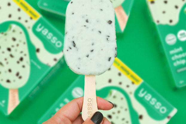 Person's hand holding an open mint chocolate chip Yasso frozen treat bar.