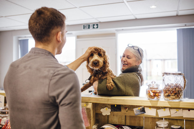Woman holding her dog at the groomer while the employee pets him.