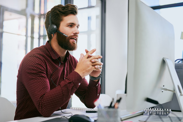 Businessman sitting sitting at desk, having discussion on a headset while using a computer in the office.