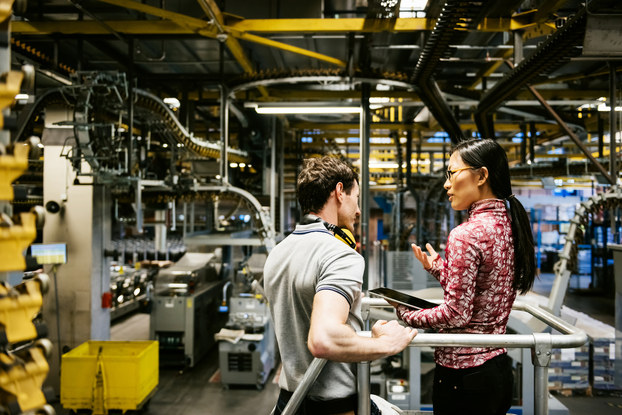 Factory mechanic and manager problem solve on a factory floor.