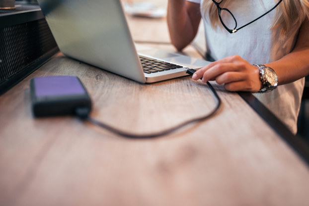 A woman plugs an external hard drive into her laptop.