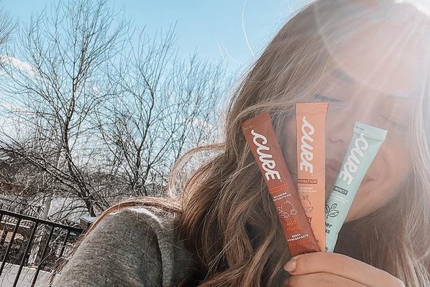 Influencer holding three Cure Hydration packets in front of her face.