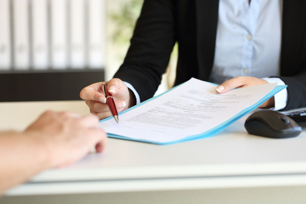 Close up of an executive hands holding a pen and indicating where to sign a contract at office.