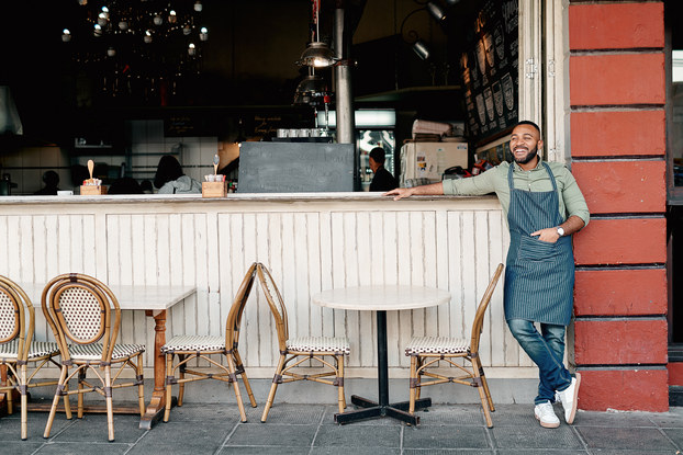 Successful entrepreneur smiles while he stands outside his cafe.