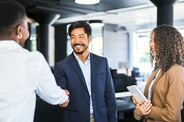 Smiling businessman shaking hands with female professional. Young businesswoman is holding digital tablet.