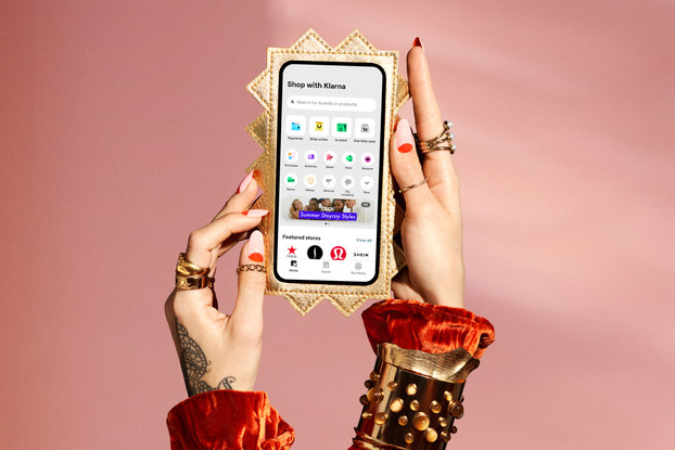 Person's hand wearing gold rings holding a phone in a spiky gold case with the Klarna app on the screen.