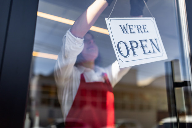 Business owner wearing a red apron and hanging a "we're open" sign in the business window.
