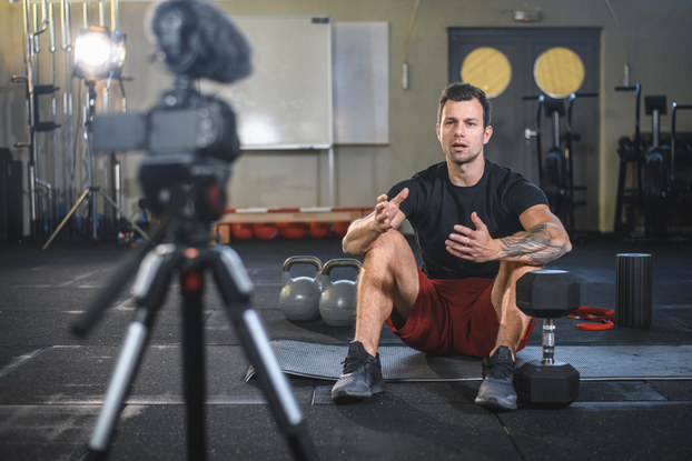 Personal Trainer films video in gym, surrounded by weights and gym equipment