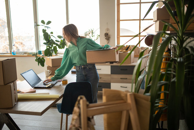 Young entrepreneur packs shipment and works on laptop to fulfill her online shop order