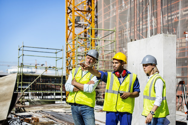 Three construction workers discuss a project on a large construction site