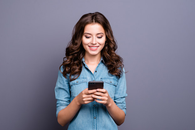 Woman standing looking at phone in front of a lilac-colored background.