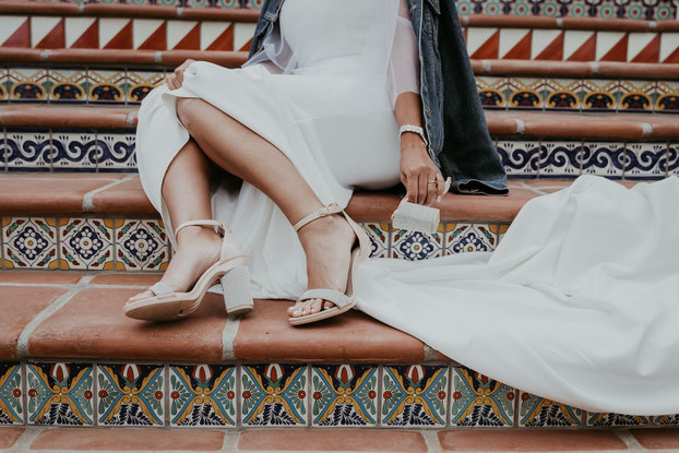 Woman sitting on stairs dressed in a formal dress with Pashion shoes on displaying the heeled and flat versions.