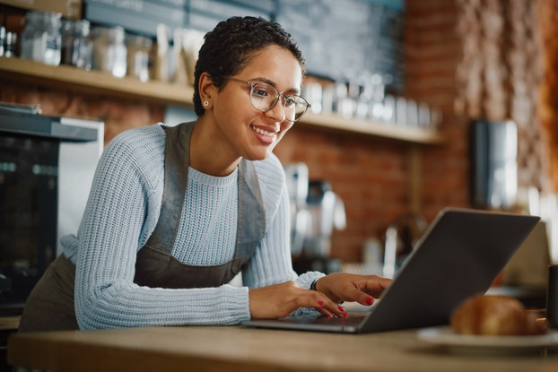 Business owner inside cafe working on laptop.