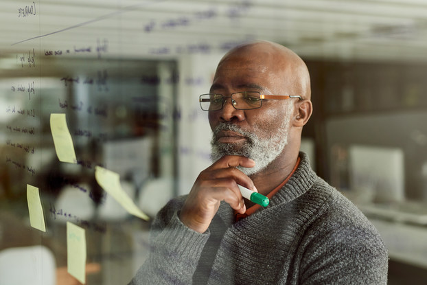 Cropped shot of a mature businessman brainstorming with notes on a glass wall