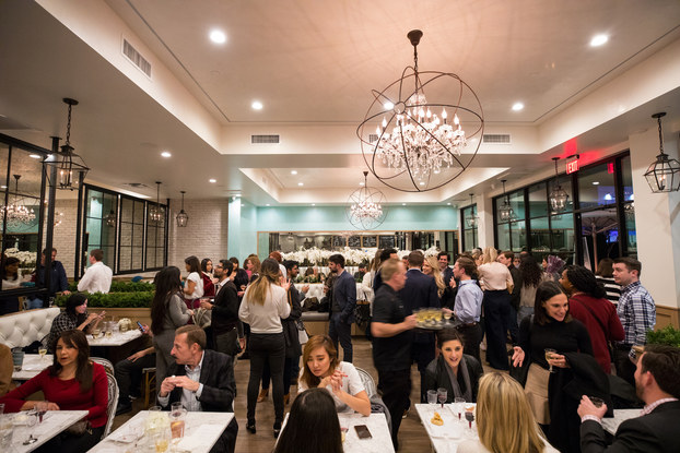 Modern restaurant with high ceilings and a chandelier is bustling with customers