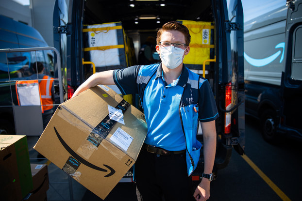 Amazon delivery driver wearing a mask and holding an Amazon package.