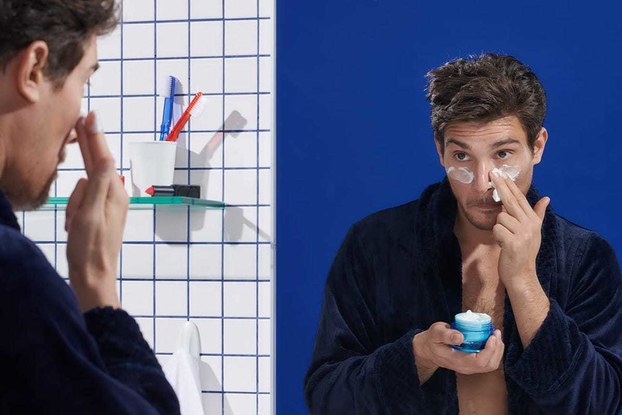 man using eye cream in bathroom mirror