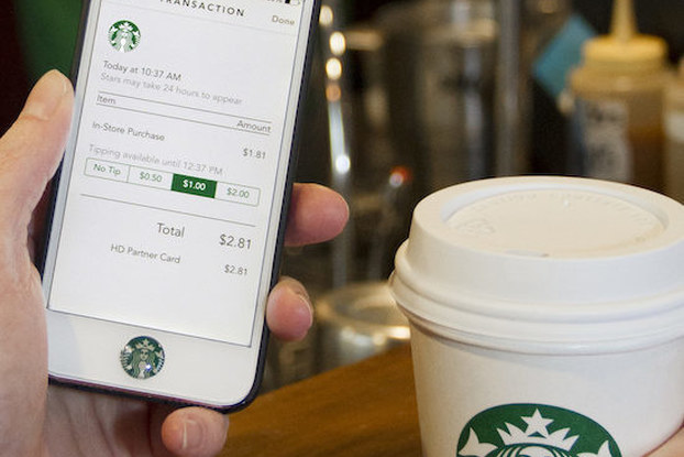 person holding starbucks cup and phone with starbucks app