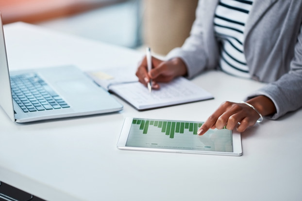 woman looking at a graph on a tablet and taking notes